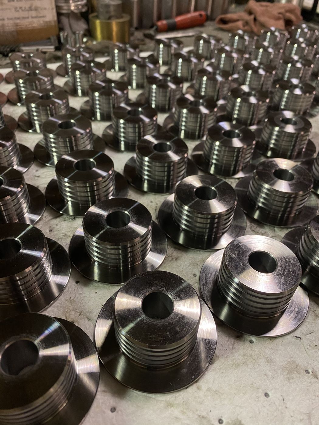 Dozens of grooved, flanged steel parts on a bench