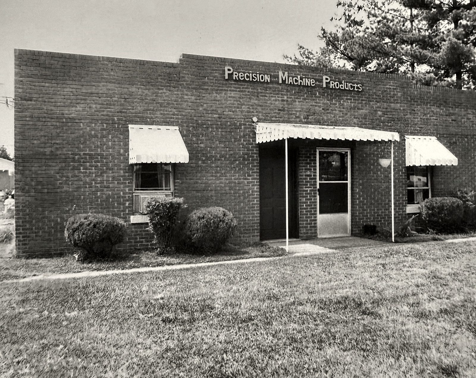 Black and white photo of a brick Precision Machine Products office with awnings