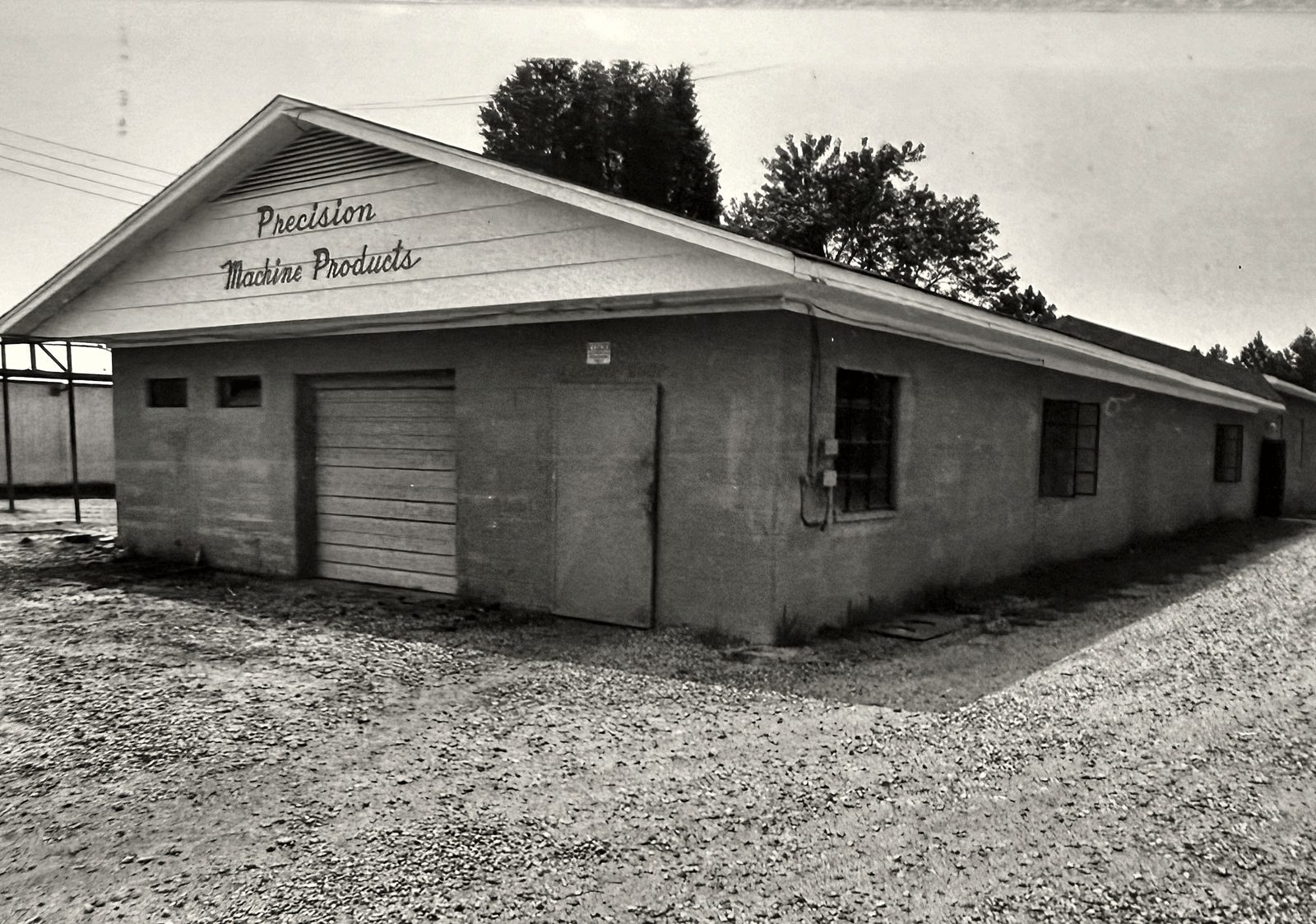 Black and white photo of an early Precision Machine Products block shop with a gable sign