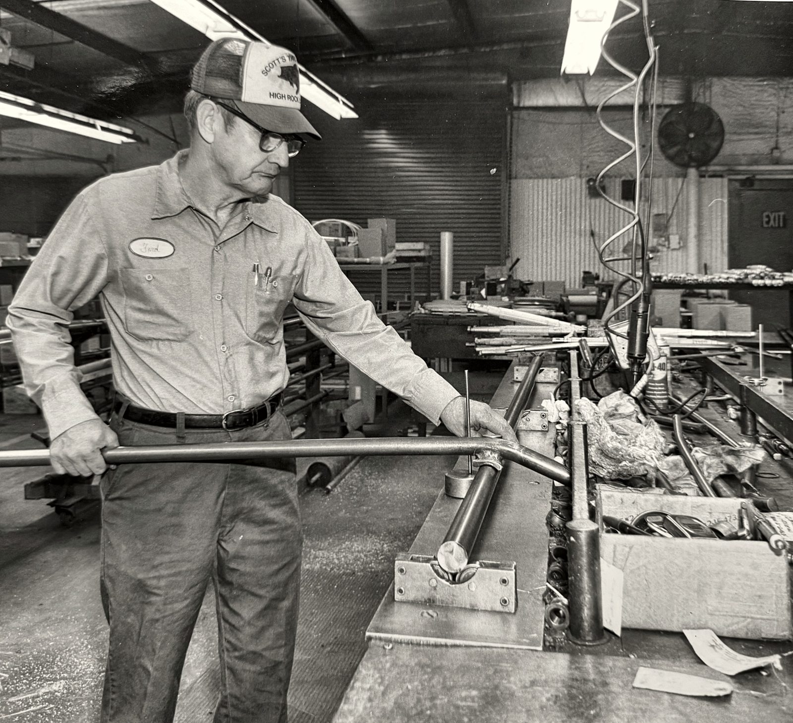 Black and white photo of a machinist bending steel tube at a workbench