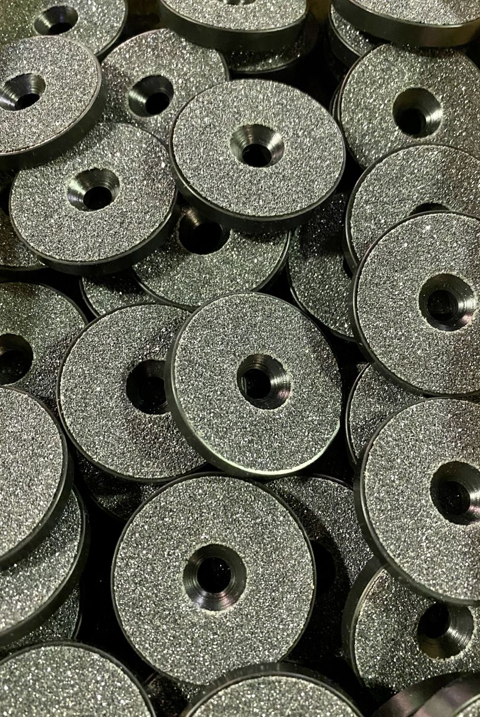 A pile of black discs with textured faces and countersunk holes